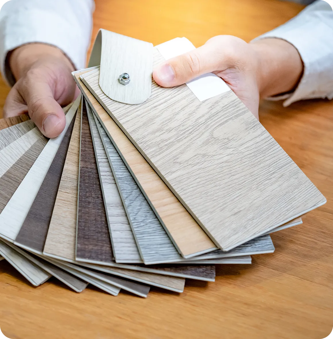 Mann hält eine Auswahl an Holzmusterproben in verschiedenen Farben auf einem Holztisch.