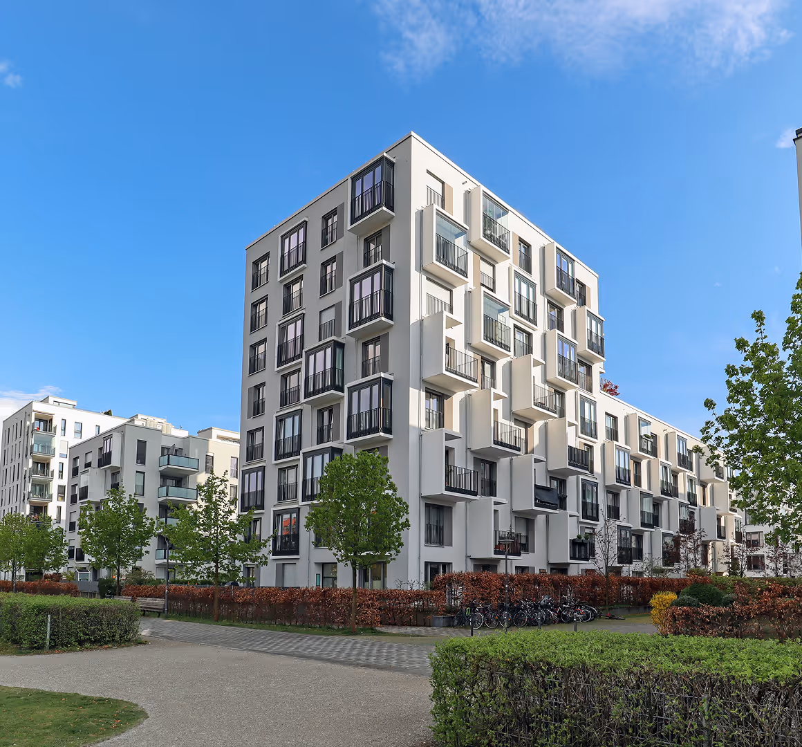 Moderne weiße Wohngebäude mit Balkonen, Bäumen und einem sonnigen blauen Himmel.