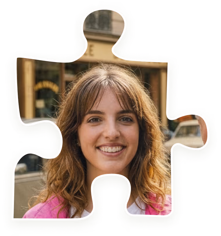 Smiling young woman with wavy brown hair wearing a pink jacket outdoors, framed in a jigsaw puzzle piece shape.