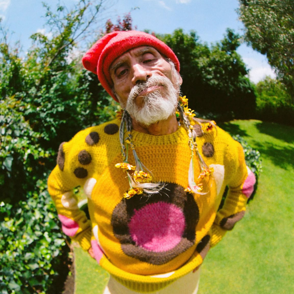 A young woman in a black blazer smiling and leaning her head toward an elderly man in glasses and a checked shirt sitting beside her outdoors.