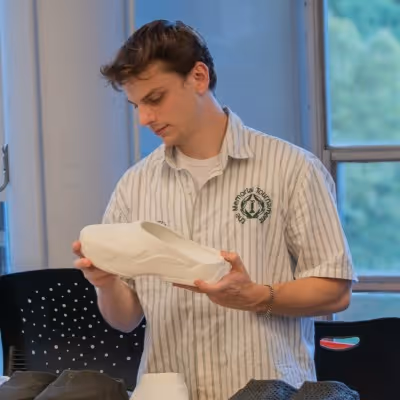 Man in a striped shirt examining a white shoe model indoors near a window.