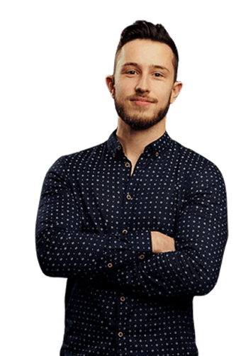 Young man with short hair and beard, wearing a dark blue patterned button-up shirt, standing with arms crossed and smiling slightly.