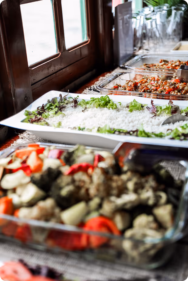Buffet table with various dishes including white rice garnished with lettuce, roasted vegetables, and a dish with diced tomatoes and mushrooms.