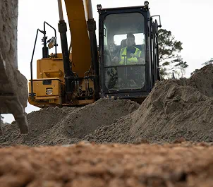 Construction vehicle with operator inside working on soil stabilization at a dirt site.