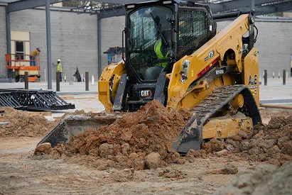 Yellow Caterpillar compact track loader moving dirt at a construction site.
