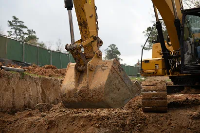 Yellow excavator with a dirt-covered bucket preparing a grading pad at a construction site.