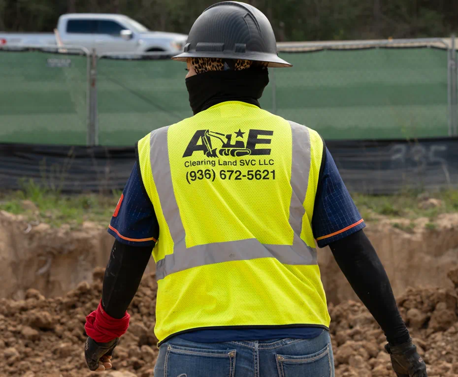 Worker wearing a yellow reflective vest and black hard hat at a construction site.