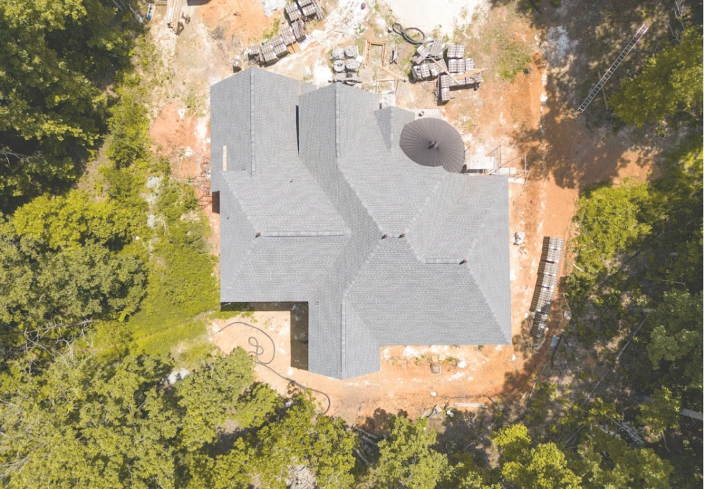 An aerial photograph showing the complex roofline of a large custom home under construction or recently completed.