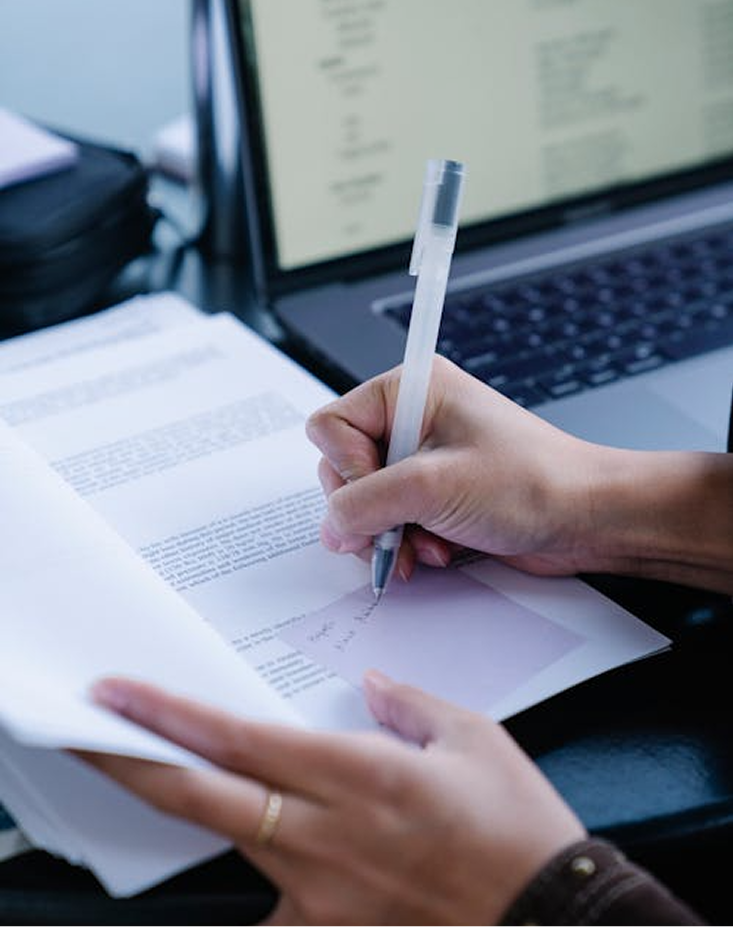 Person writing notes on a sticky note inside an open book, with a laptop keyboard visible in the background.
