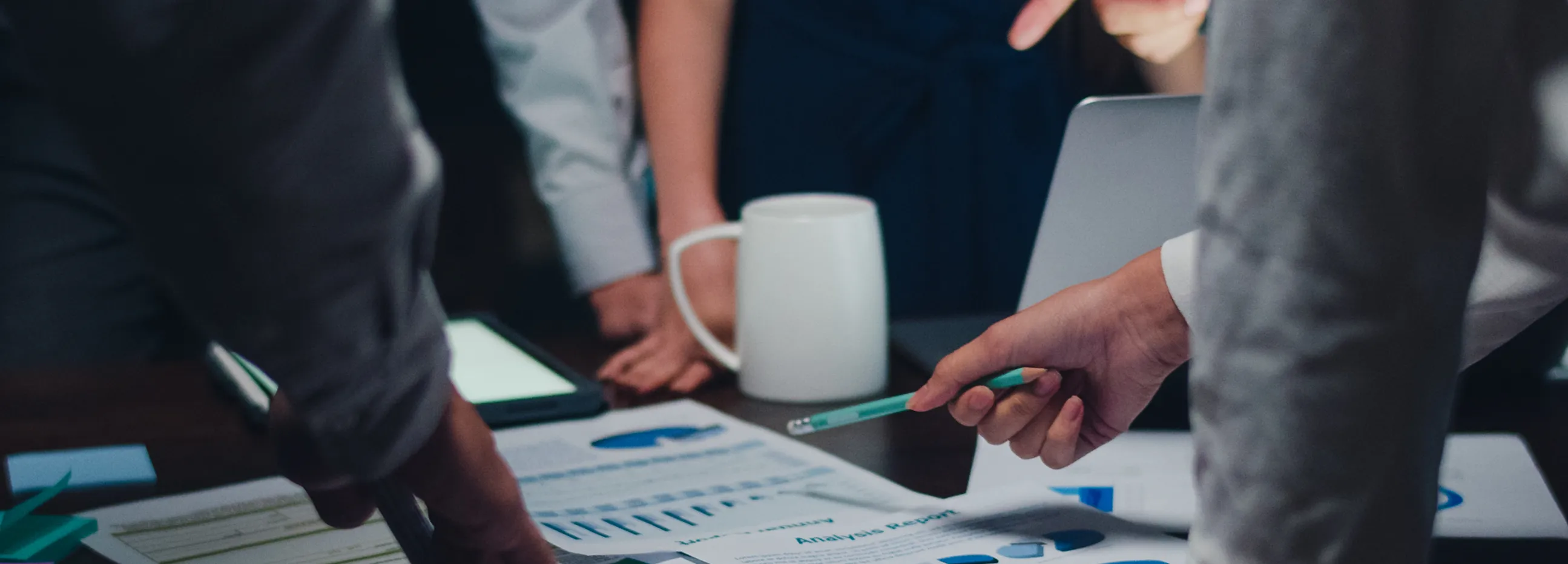 Close-up of hands pointing at printed charts and graphs on a table during a business meeting.