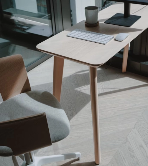 Minimalist workspace with a wooden desk holding a keyboard, mouse, and coffee cup next to a gray cushioned office chair.