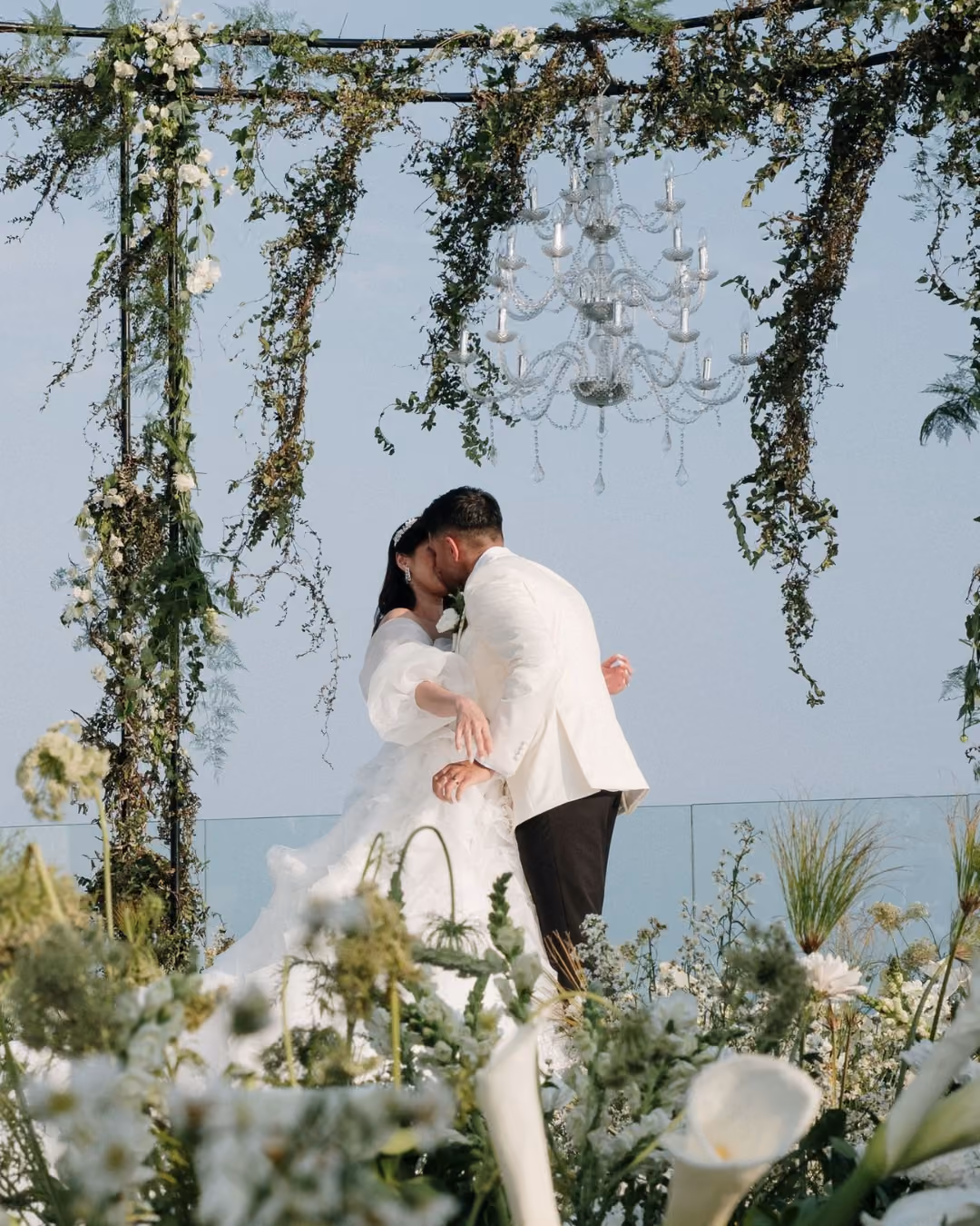 Couple sharing a kiss under a floral arch with a chandelier