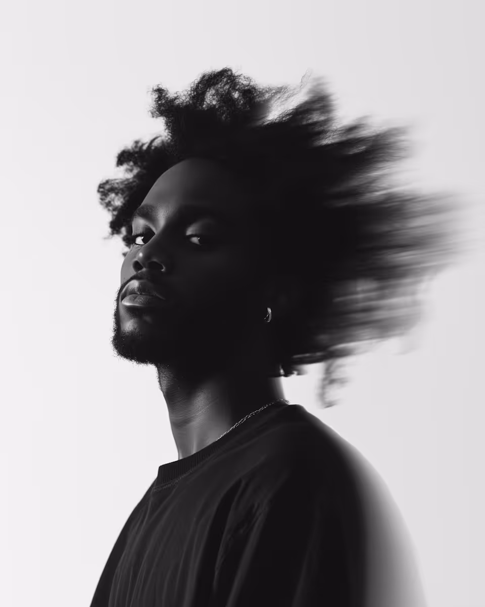 Black and white portrait of a man with afro hair blurred in motion against a light background.
