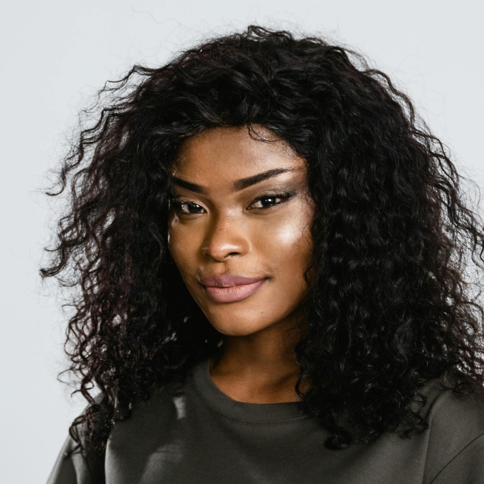 Close-up of a confident woman with curly black hair wearing a dark grey top against a light background.