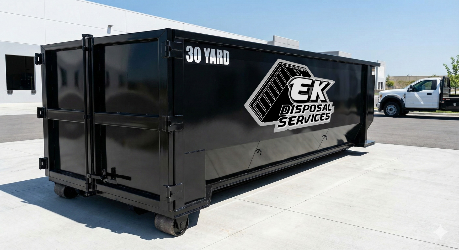 Large black 30-yard dumpster with EK Disposal Services logo, parked on a concrete surface near a white pickup truck and buildings.