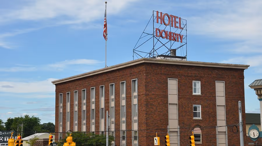 Brick building with 'Hotel Doherty' sign on top and an American flag on a flagpole, under a partly cloudy blue sky.