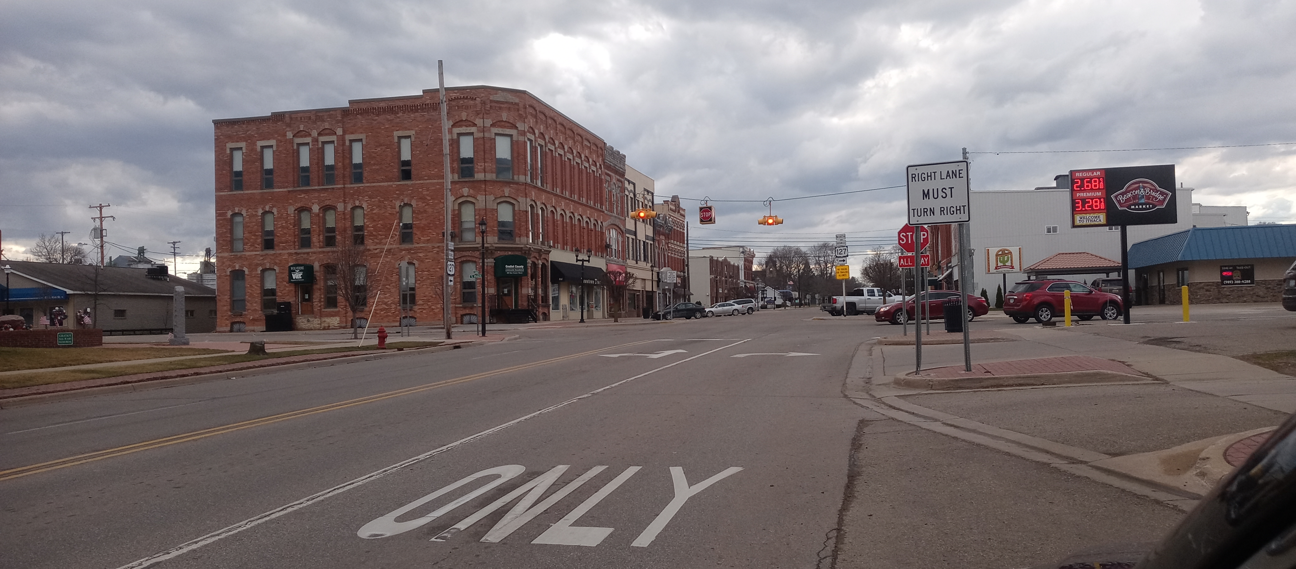 Downtown street scene with historic red brick buildings, traffic lights, and a gas station under cloudy sky.
