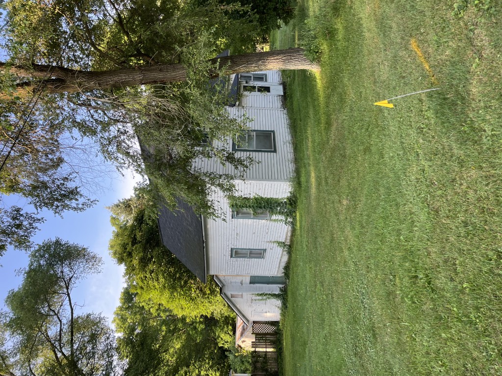 White farmhouse with green trim surrounded by trees and lawn with a small yellow flag on a stick in the grass. EK Disposal Services Demolition Services