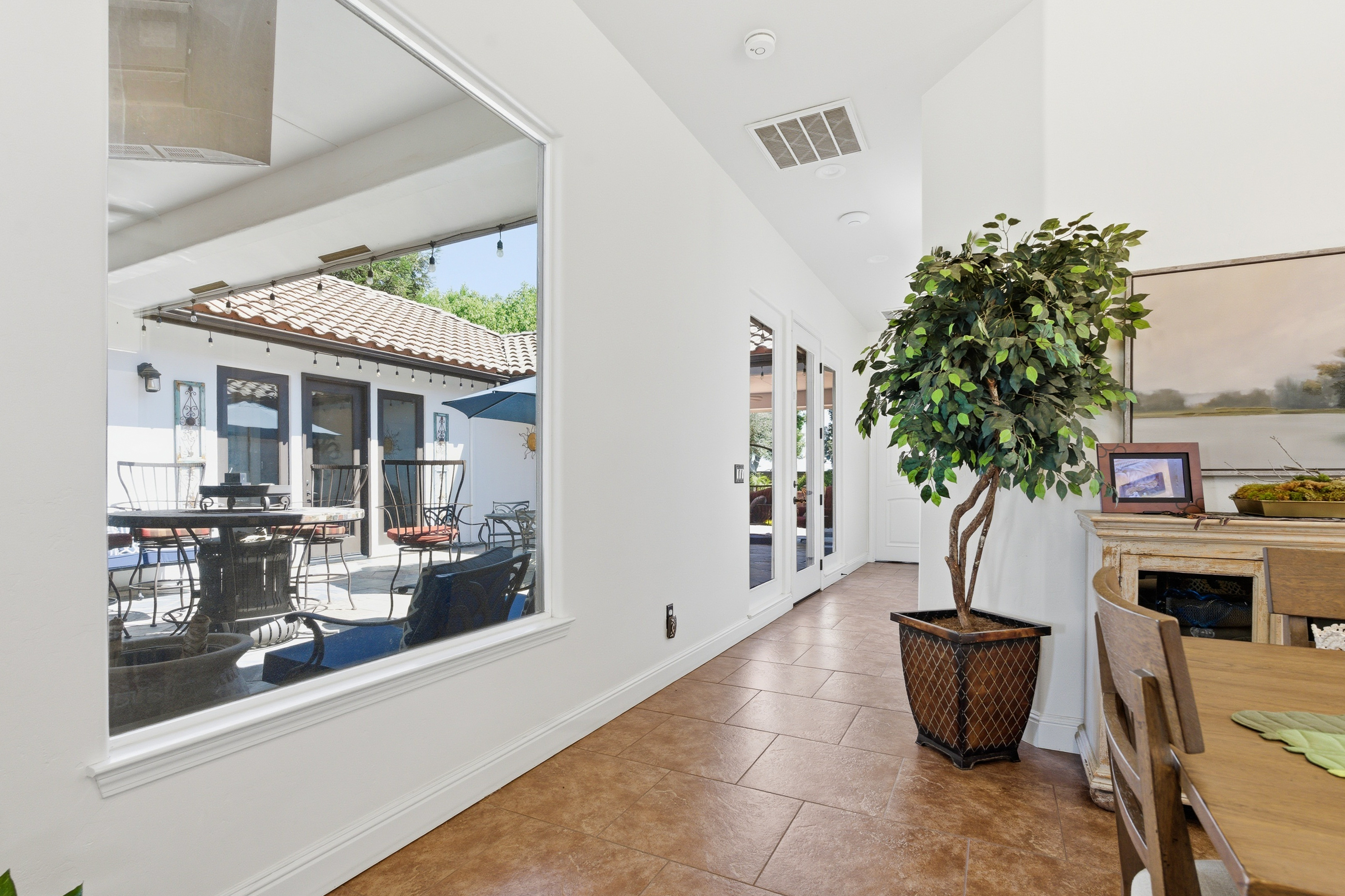 Indoor hallway with large window showing outdoor patio with chairs, table, and umbrella.