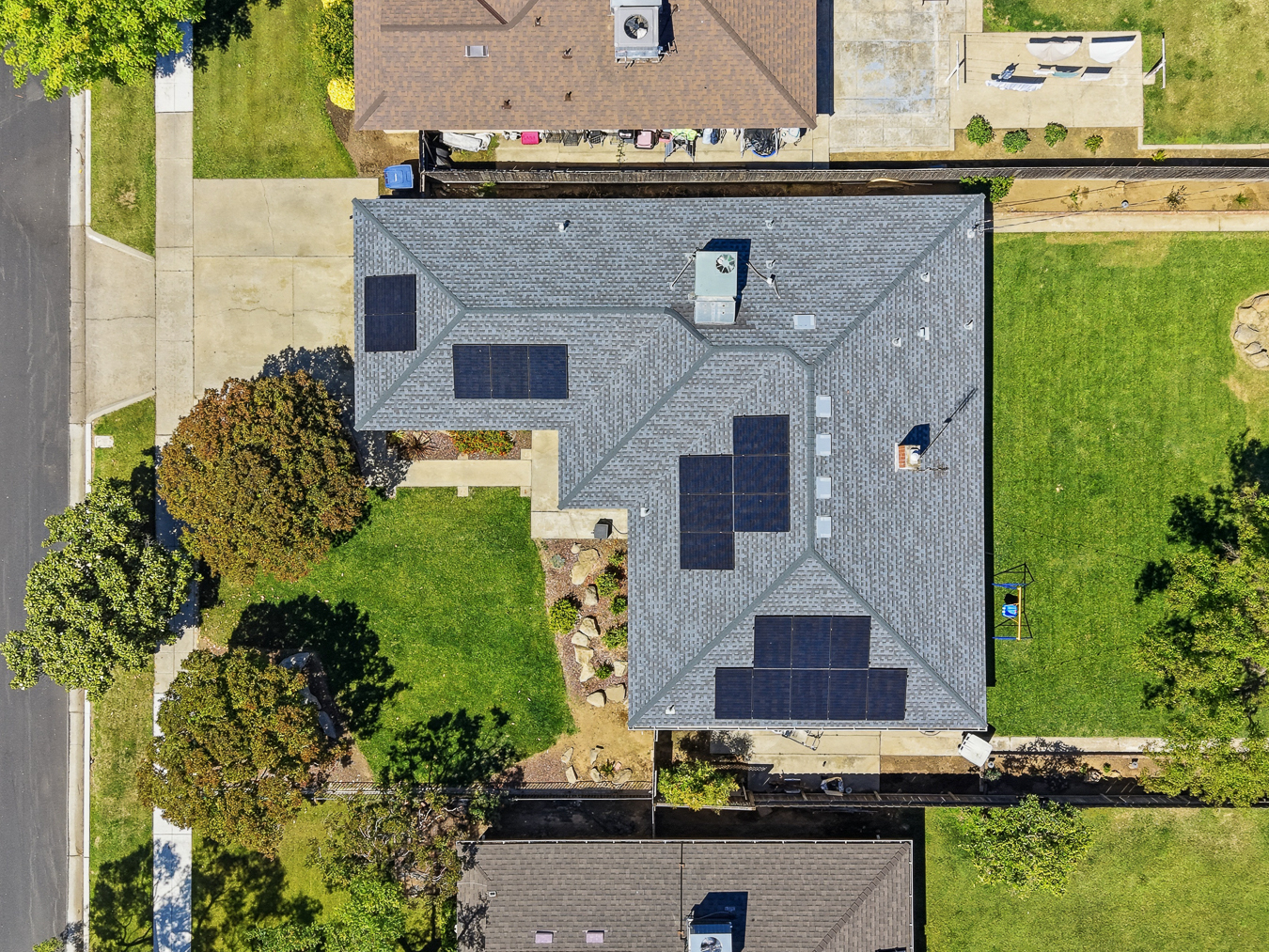 Aerial view of a house with multiple solar panels on its roof and green lawns on both sides.