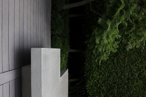 Modern concrete bench on wooden deck surrounded by lush green bushes and trees.