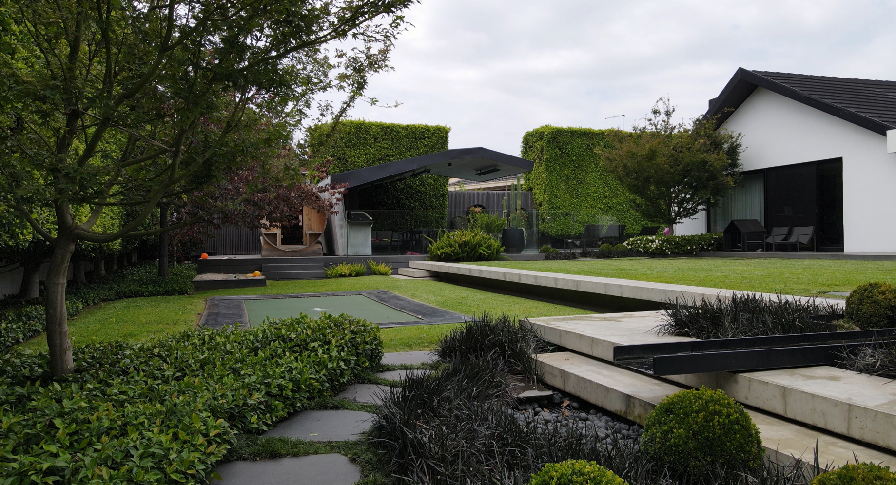 Modern formal garden with manicured hedges, geometric lawn, concrete steps and contemporary pavilion in a premium Brighton estate