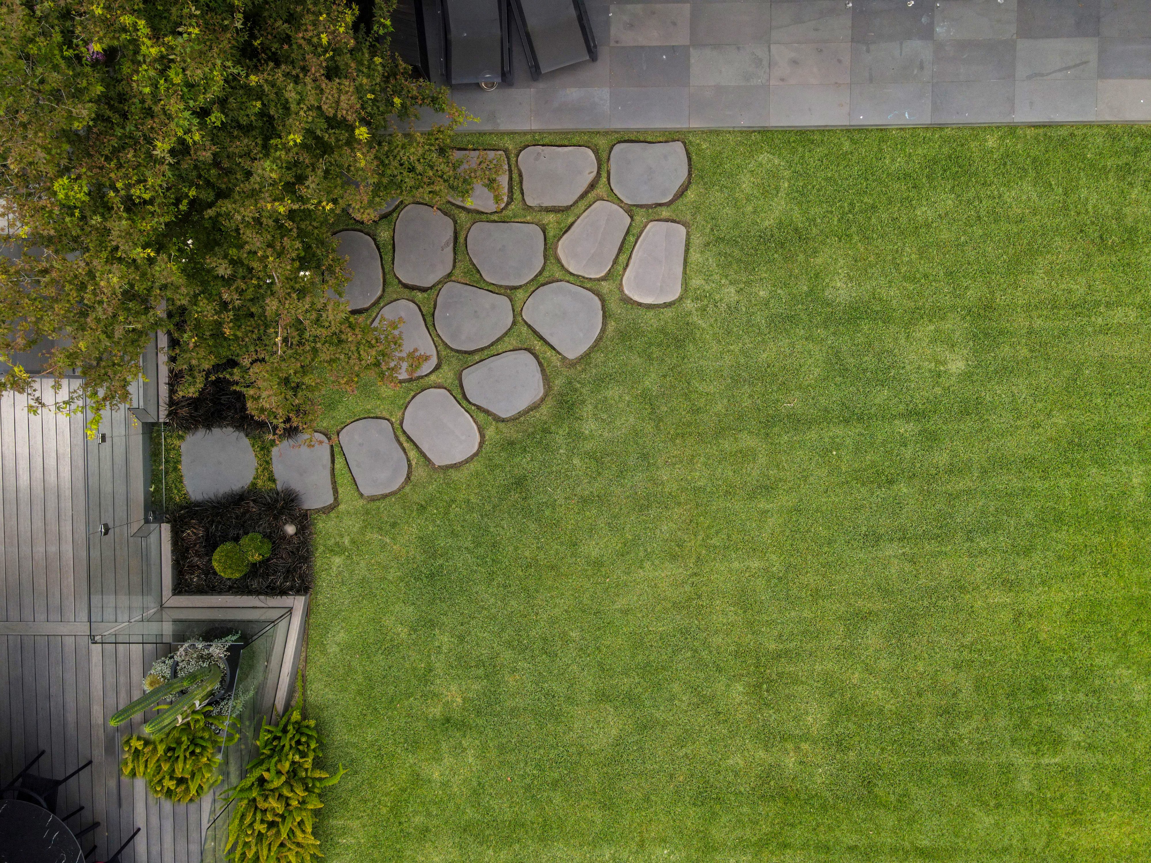 Drone view of manicured lawn with natural stepping stone path and modern deck in a Toorak garden