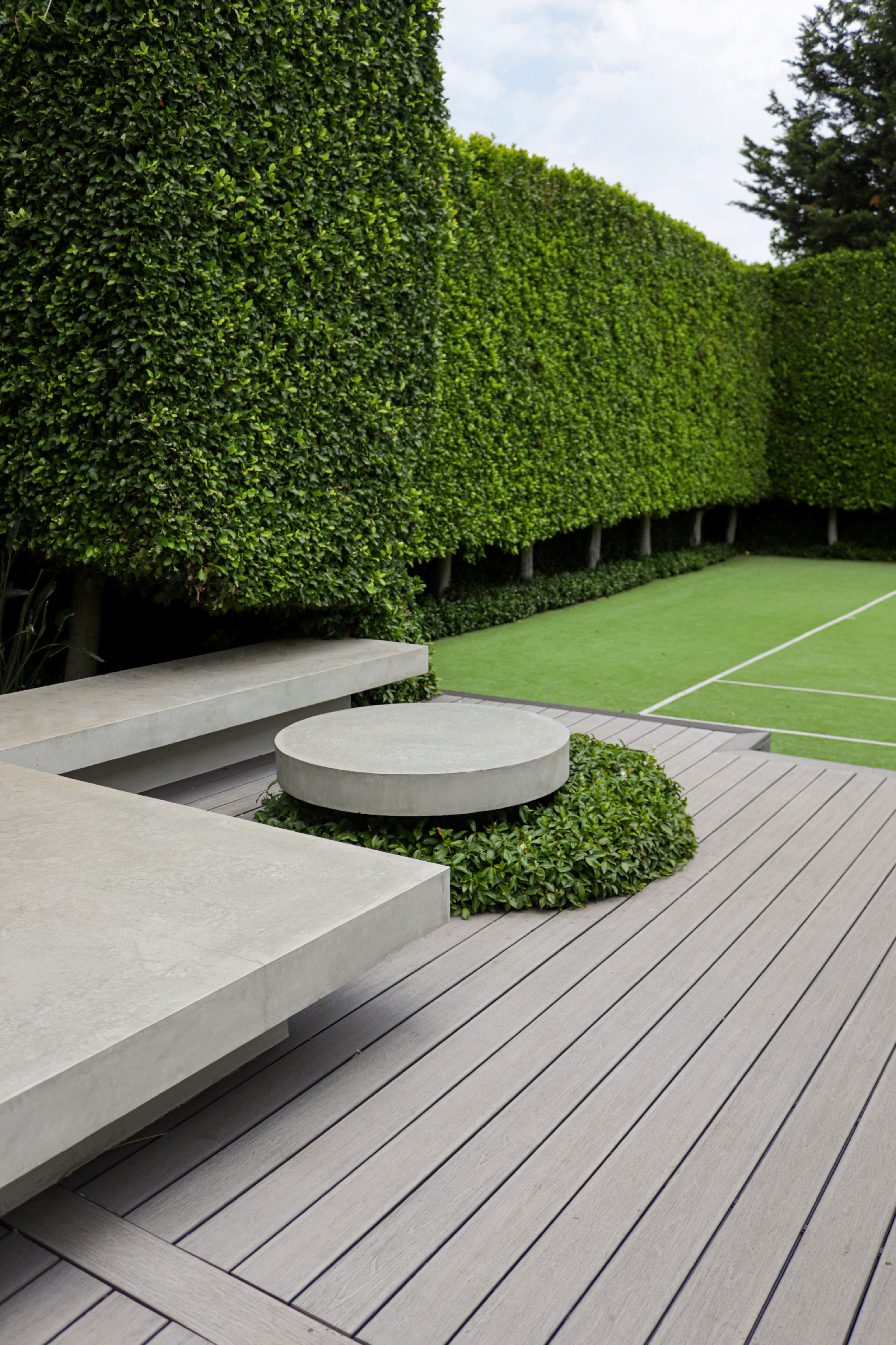 Modern timber deck with concrete benches and circular table surrounded by perfectly manicured formal hedges in a Toorak estate garden