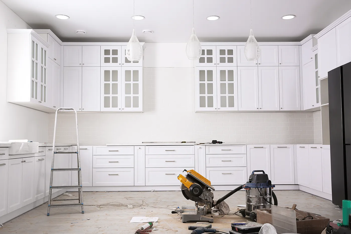 Florida Building Contractors ongoing kitchen remodel in Tampa Bay area showing newly installed white shaker cabinets, pendant lights, and construction tools including miter saw and shop vacuum on site.