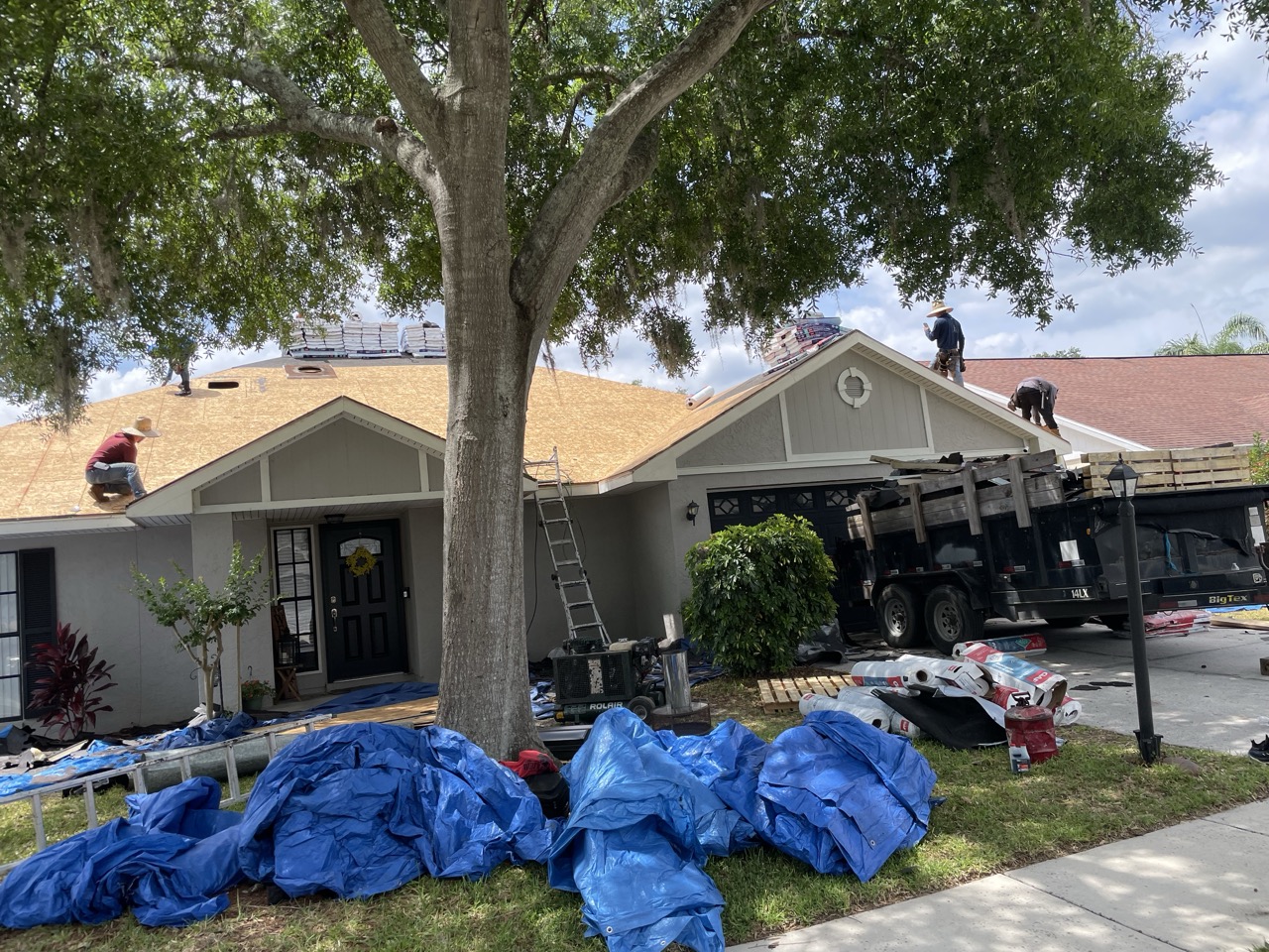 Florida Building Contractors crew preparing and installing new roofing on a single-story Florida home, with workers on the partially completed roof, ladders, tarps, materials, and debris containers surrounding the house under sunny skies.