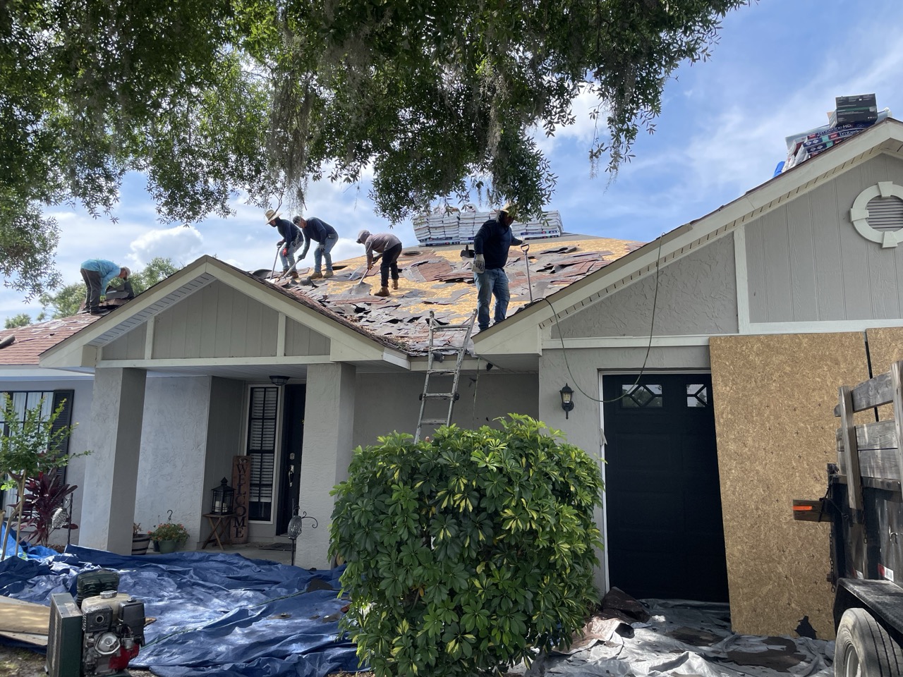 Workers from Florida Building Contractors removing old, damaged roofing shingles during tear-down phase on a single-story home's roof in Florida, with ladders, tools, and materials on site under a sunny sky.