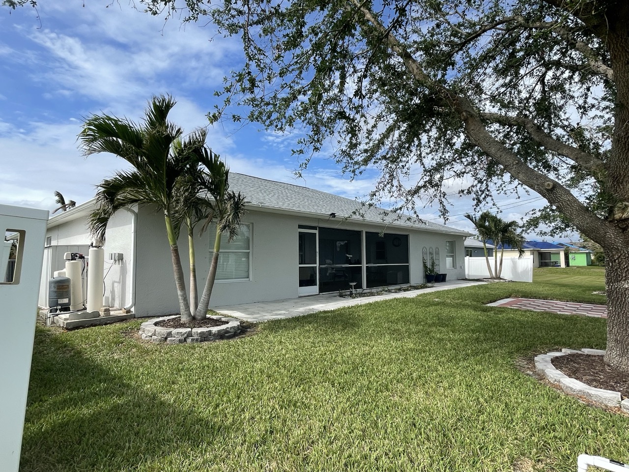 Completed roof replacement by Florida Building Contractors on a modern single-story Florida home with gray asphalt shingles, white stucco exterior, palm trees, and covered entryway under clear blue skies.