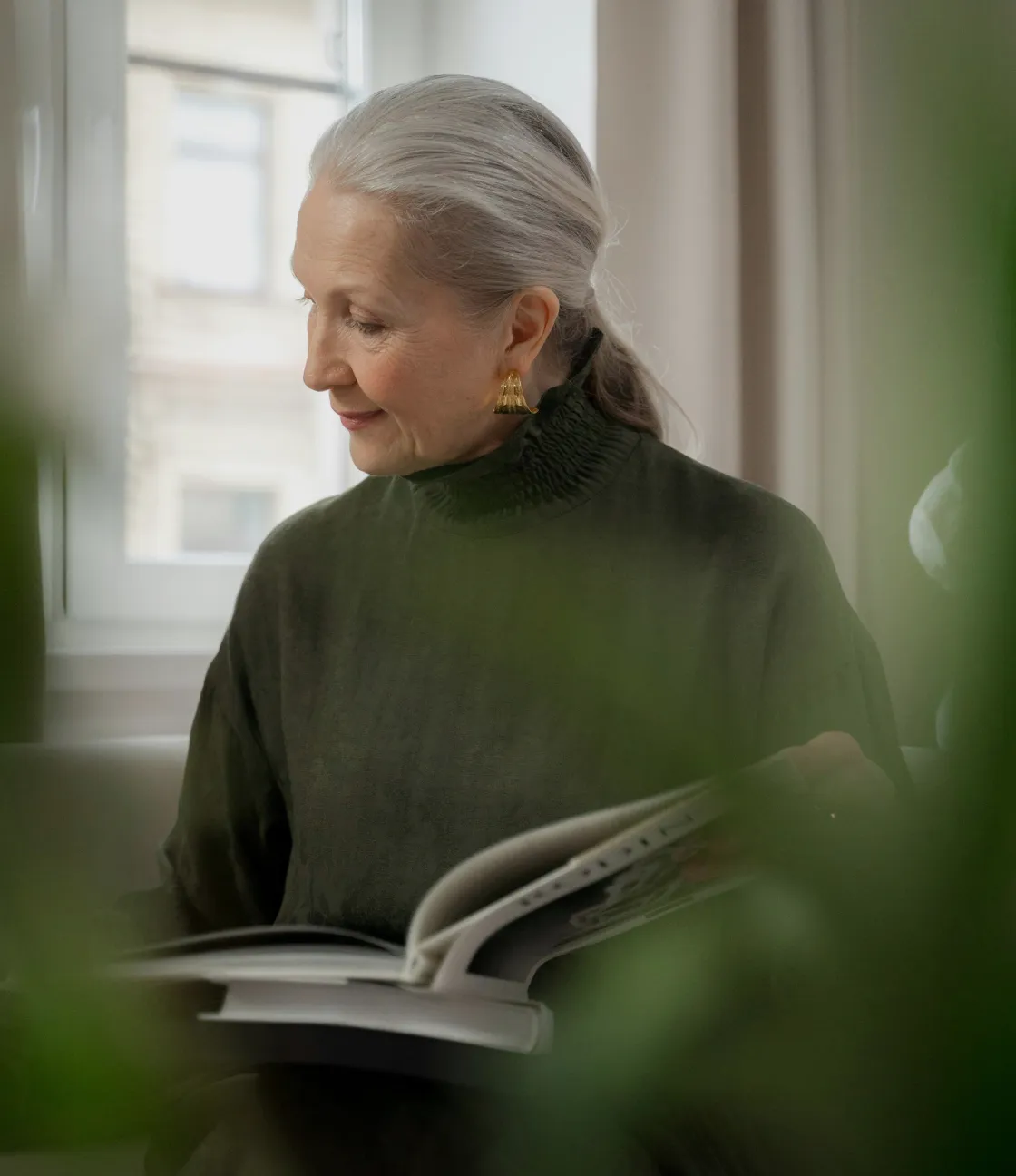 An older woman reading a book near a window