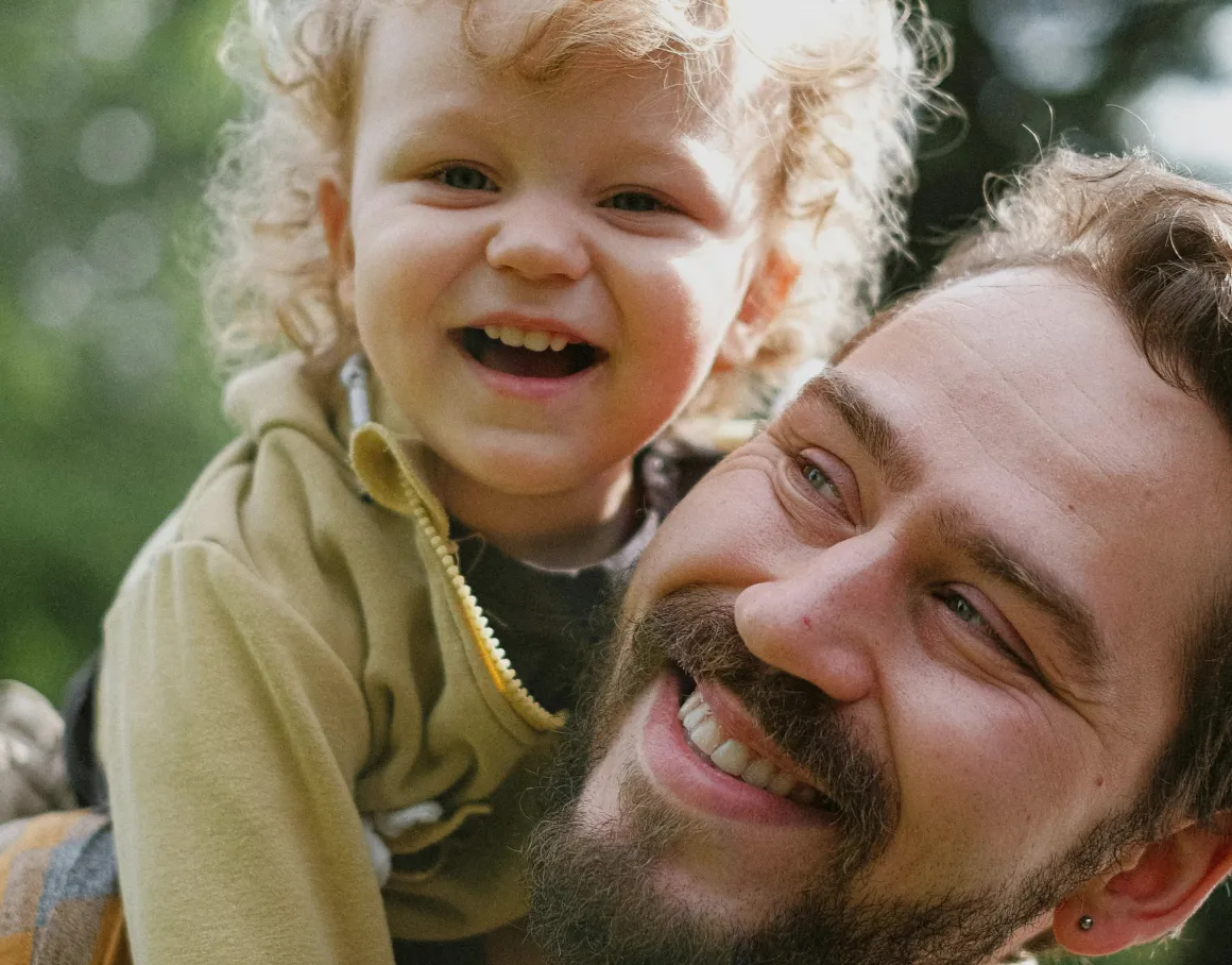 A parent smiling while holding a young child outdoors