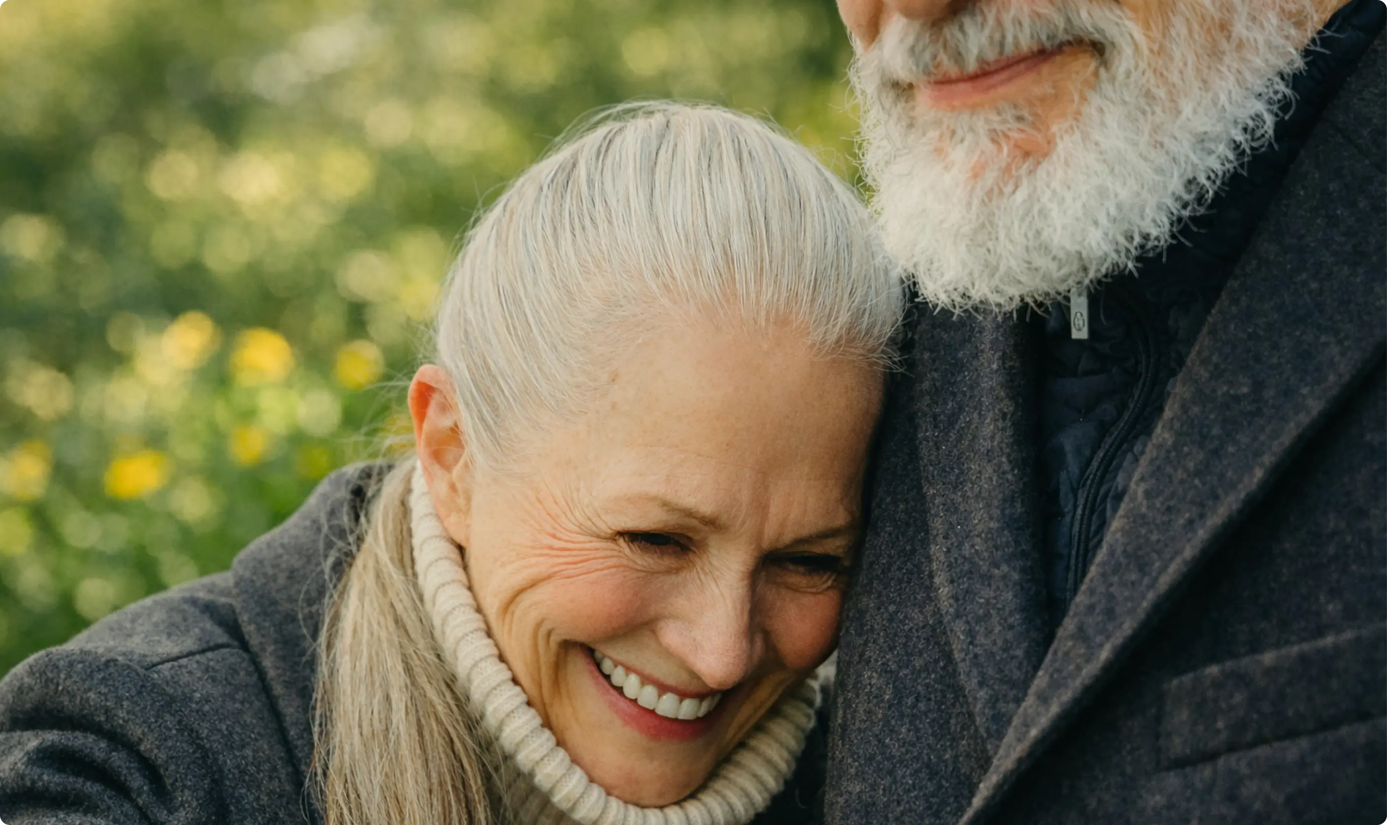 An older woman smiling while leaning into a man’s chest outdoors.