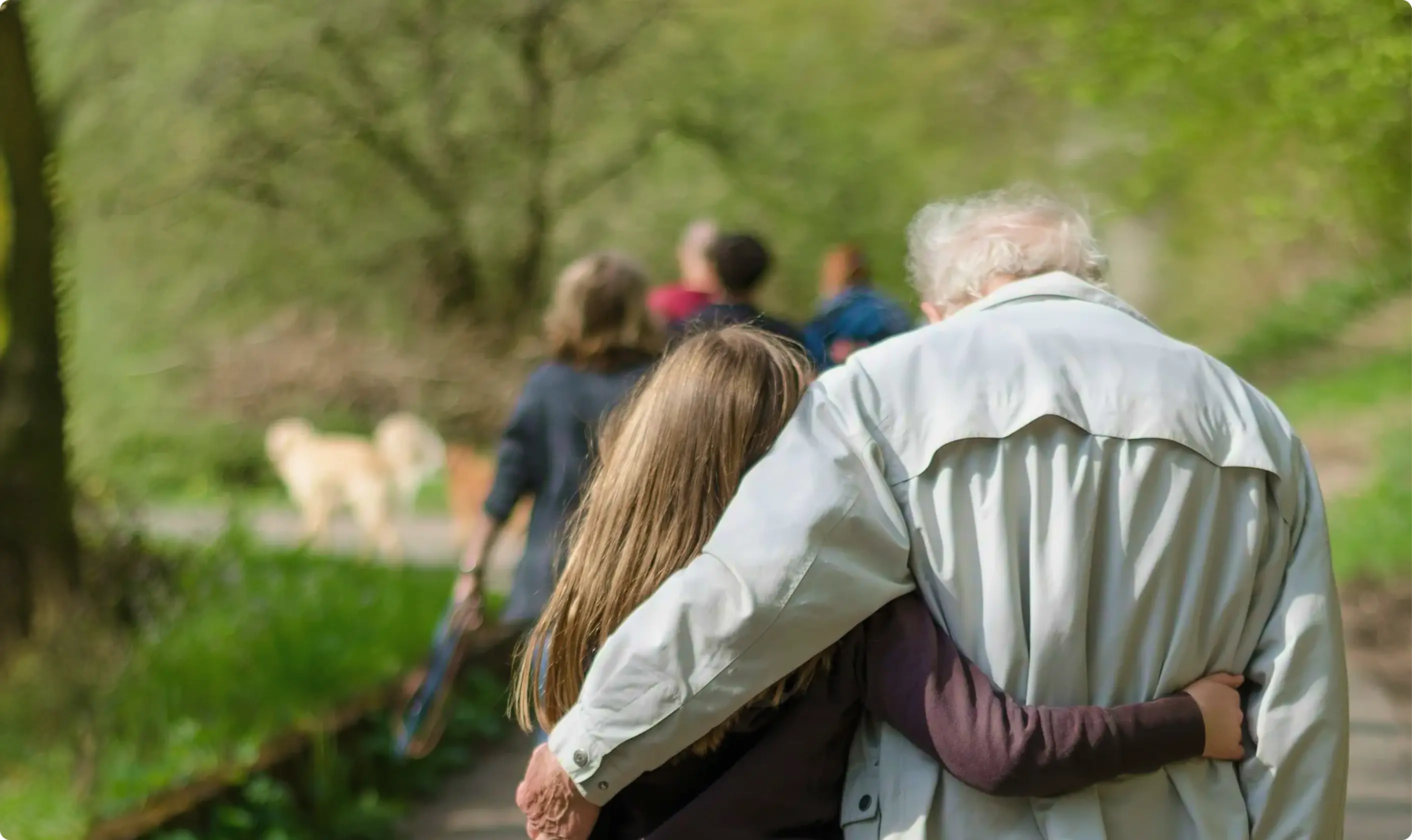 An elderly person walking arm in arm with a younger person along a park path.