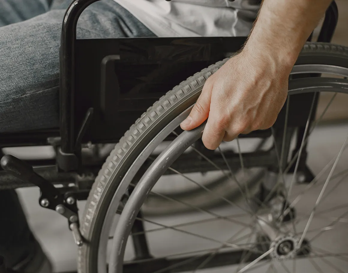 A close-up of a person’s hand gripping the wheel of a wheelchair.