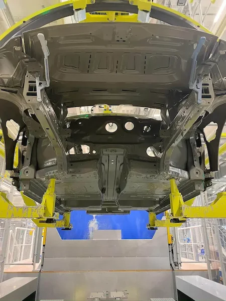 Pogled od spodaj na karoserijo avtomobila vpeto v rumen Eisenmann rotacijski sistem med postopkom lakiranja