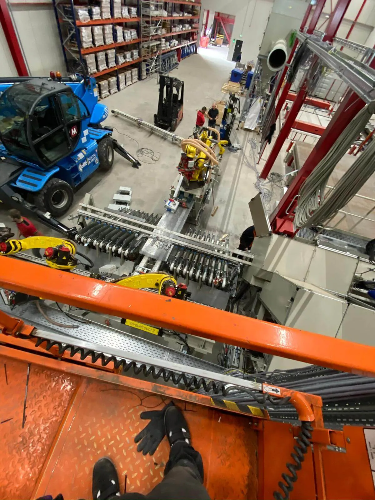 Pogled z višine na montažo avtomatizirane proizvodne linije z rumenimi Fanuc roboti in viličarjem med namestitvijo opreme v industrijski hali