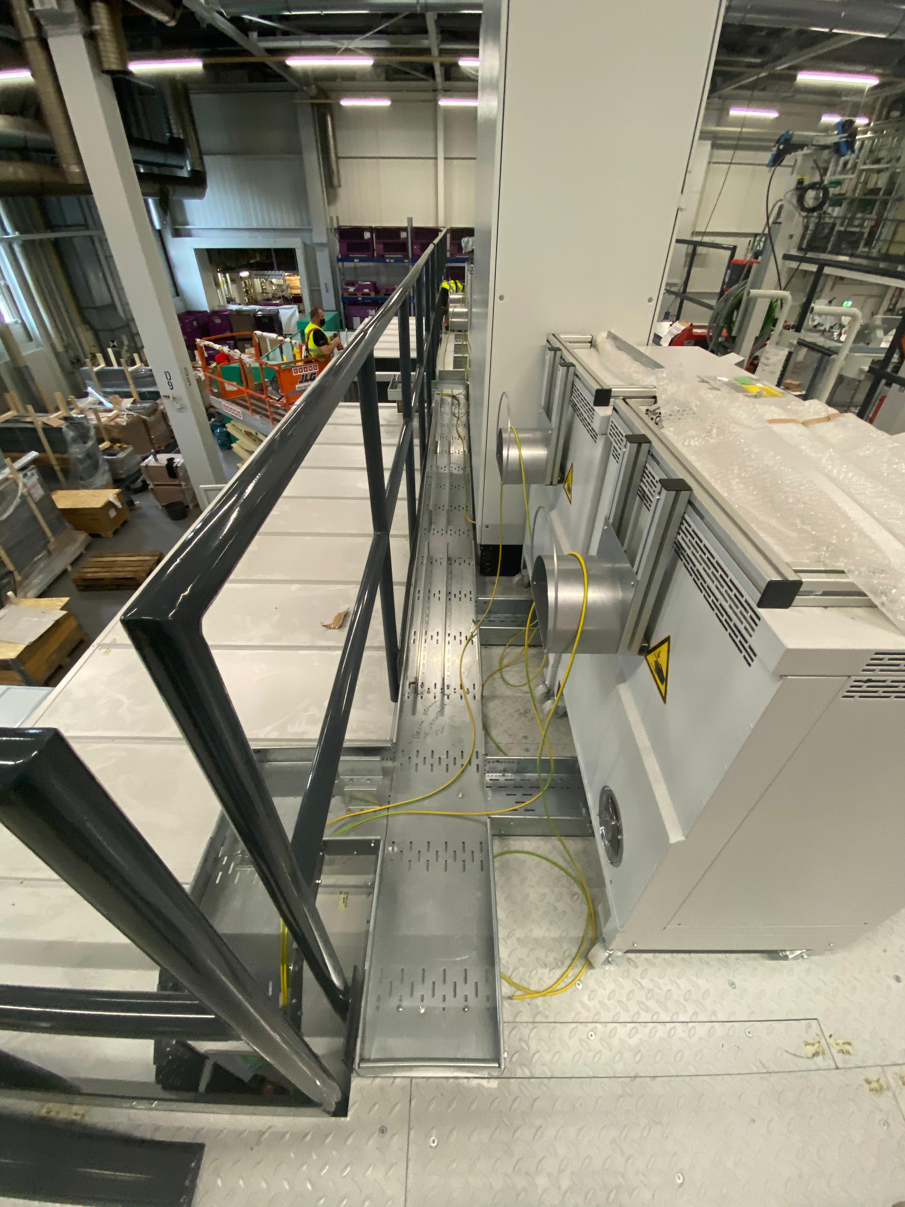 Montaža industrijskih razvodnih omarov ob servisni ploščadi z rumenimi ozemljitvenimi kabli v proizvodni hali