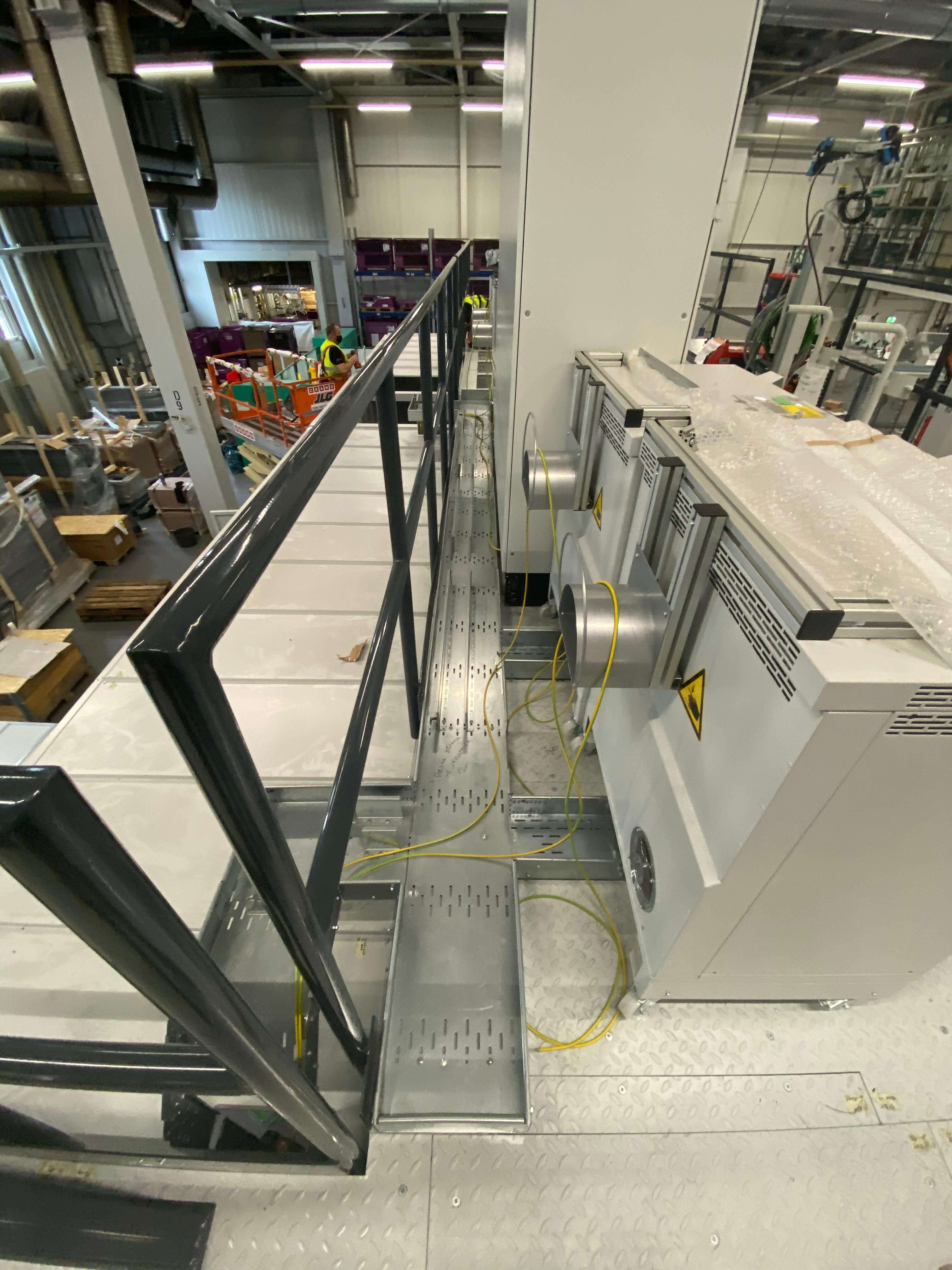 Montaža industrijskih razvodnih omarov ob servisni ploščadi z rumenimi ozemljitvenimi kabli v proizvodni hali