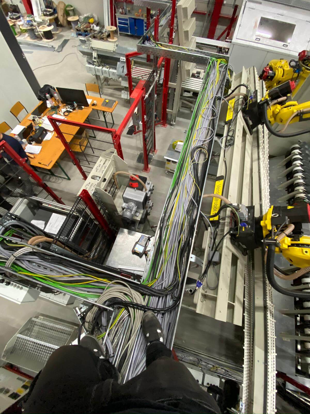 Pogled z višine na kabelski razvod sivih in zeleno-rumenih ozemljitvenih kablov vzdolž proizvodne linije z rumenimi Fanuc roboti