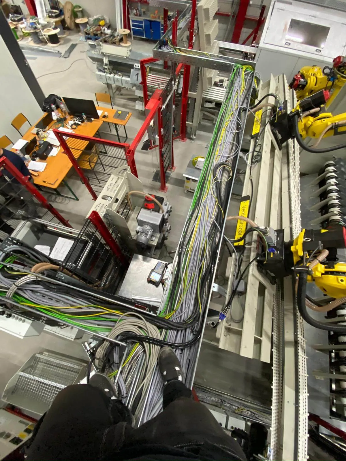 Pogled z višine na kabelski razvod sivih in zeleno-rumenih ozemljitvenih kablov vzdolž proizvodne linije z rumenimi Fanuc roboti