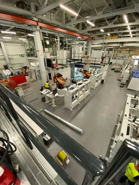 Pogled od zgoraj na industrijsko halo z več KUKA robotskimi rokami oranžne barve na avtomatizirani proizvodni liniji