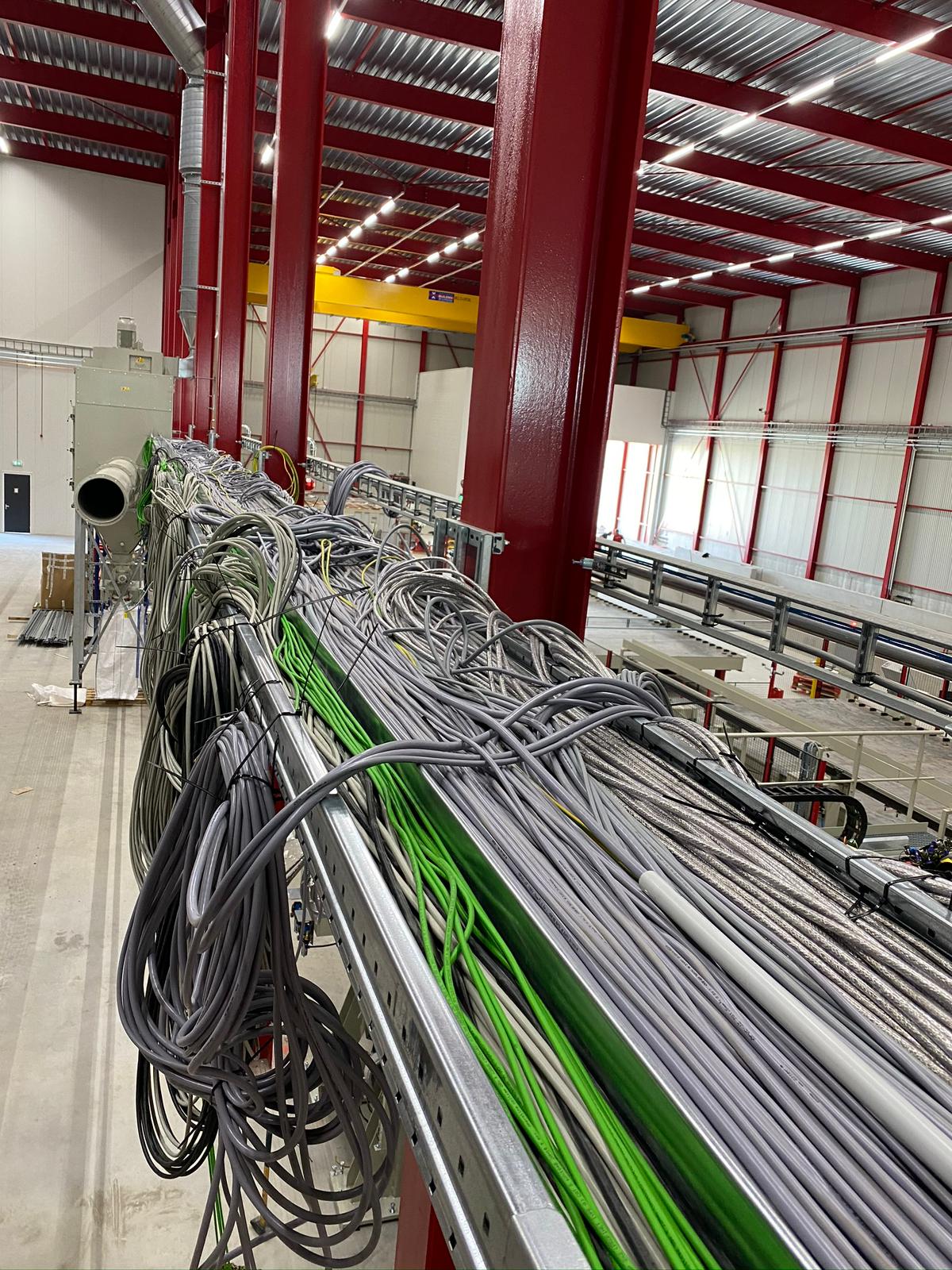 Kabelski most z množico sivih in zelenih PROFINET kablov v industrijski hali z rdečo jekleno konstrukcijo
