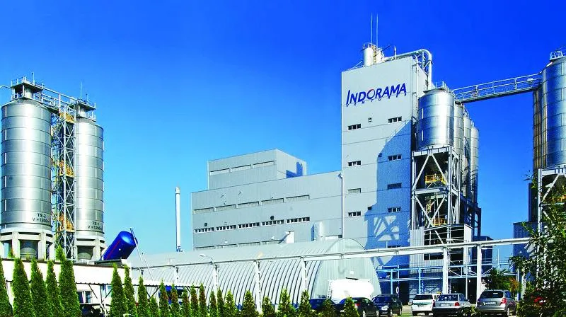 Industrijski obrat z velikimi jeklenimi rezervoarji in stavbo z napisom Indorama pod modrim nebom.
