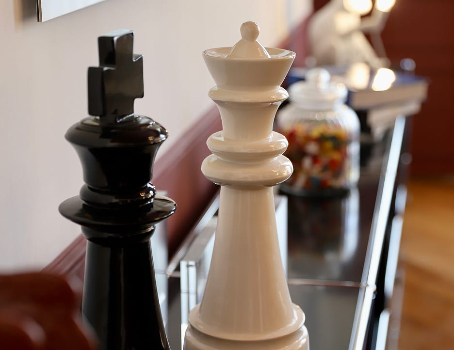 Large black and white chess king pieces placed on a reflective surface with a blurred background including a jar of colorful candies.