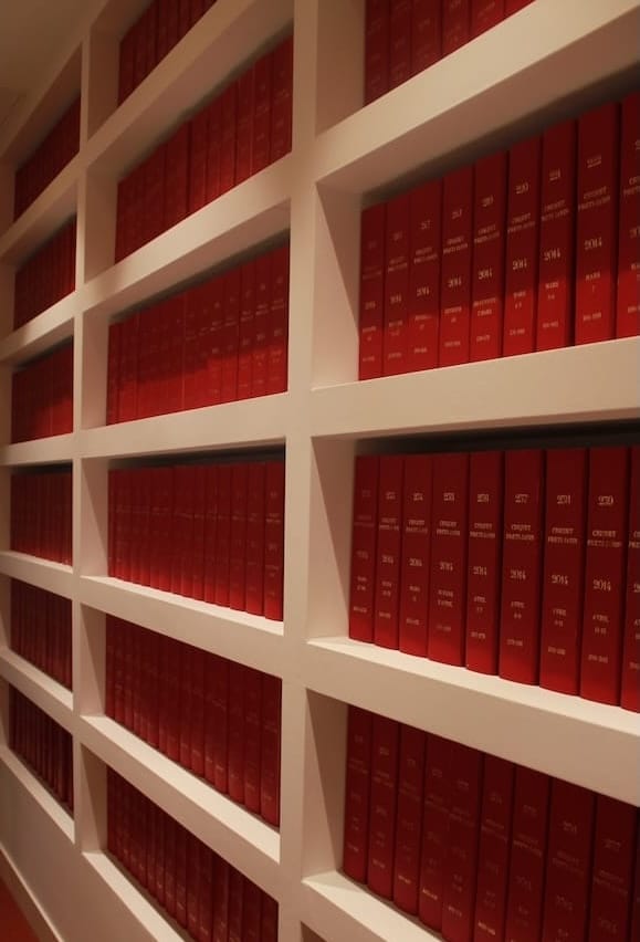 Shelves filled with multiple rows of red hardcover books with gold text on the spines.