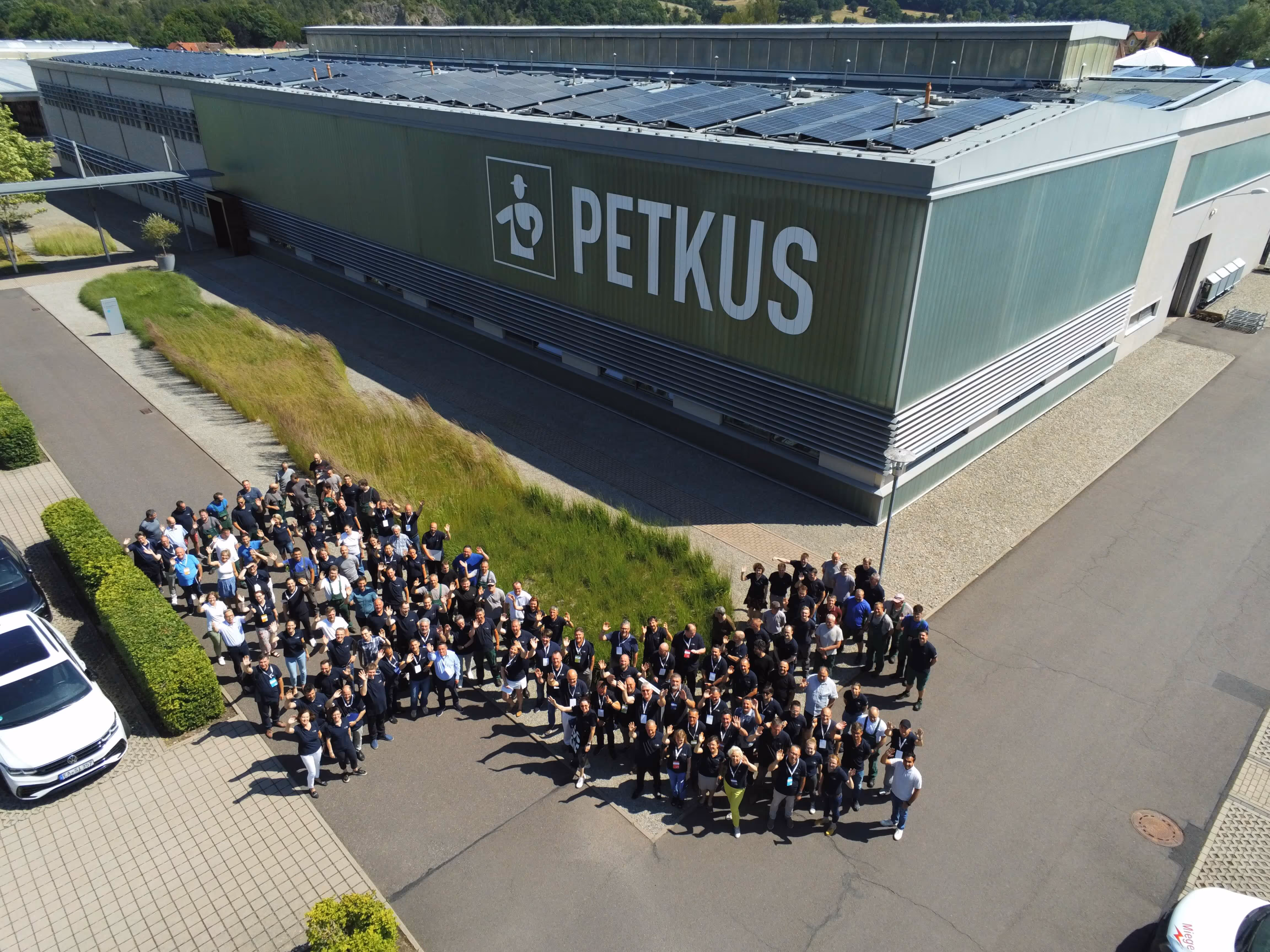 Large group of people standing outside a green industrial building with PETKUS logo on the side.