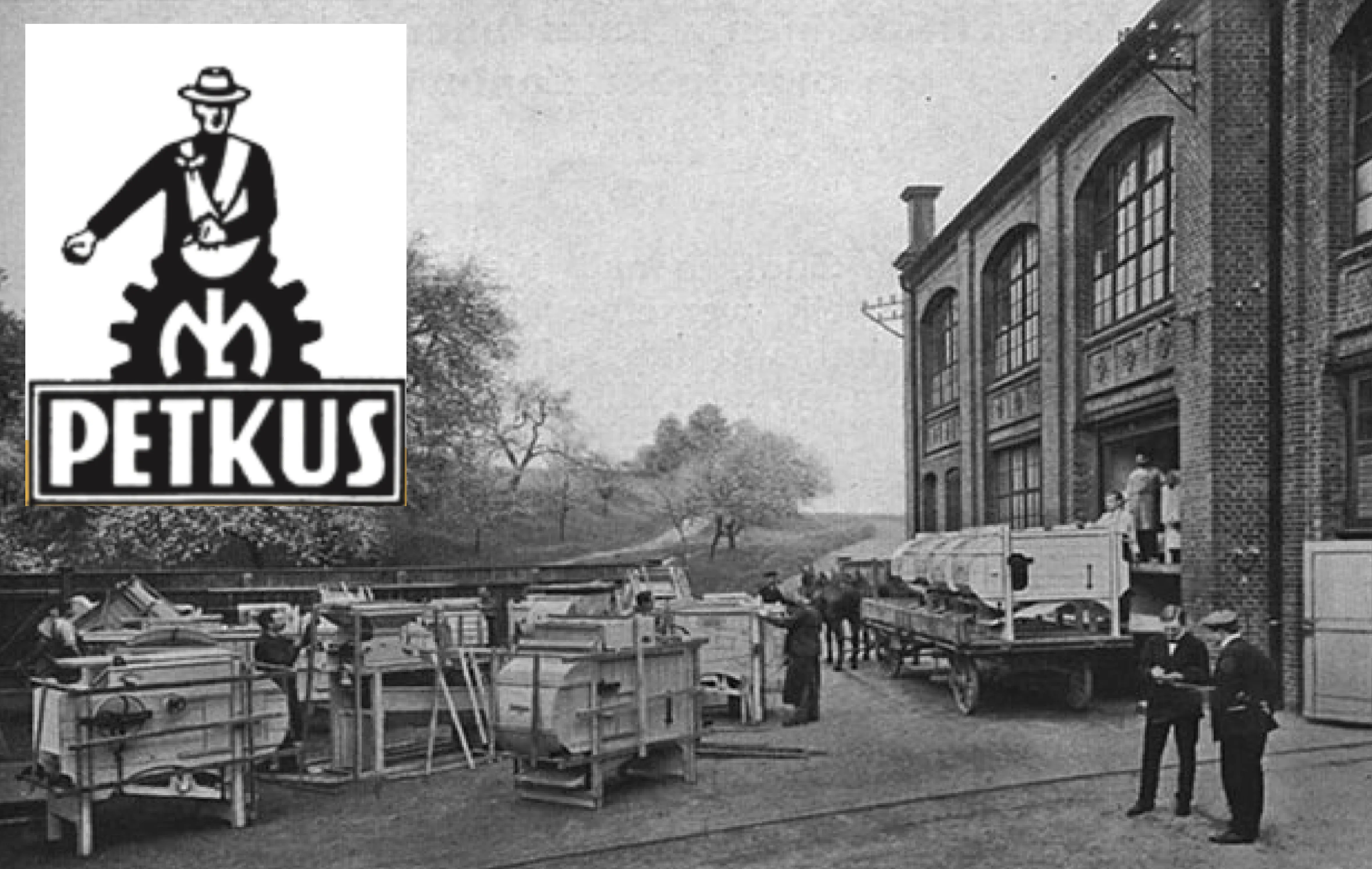 Black and white historical photo showing a group of workers handling large wooden crates outside a brick industrial building with large windows, a horse-drawn cart loaded with crates, and two men conversing in the foreground; an inset logo in the top left corner depicts a man with a hat inside a gear with the word PETKUS below.